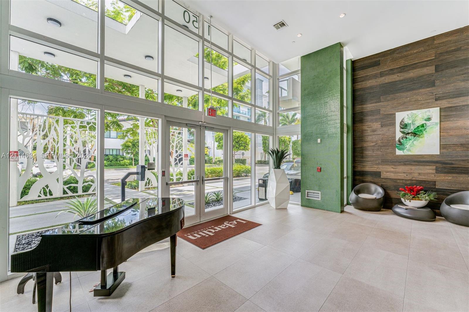 Grand entrance lobby featuring double-height glass curtain walls, floor-to-ceiling windows, large-format tile flooring, a vibrant green accent pillar, and horizontal wood-finish wall paneling