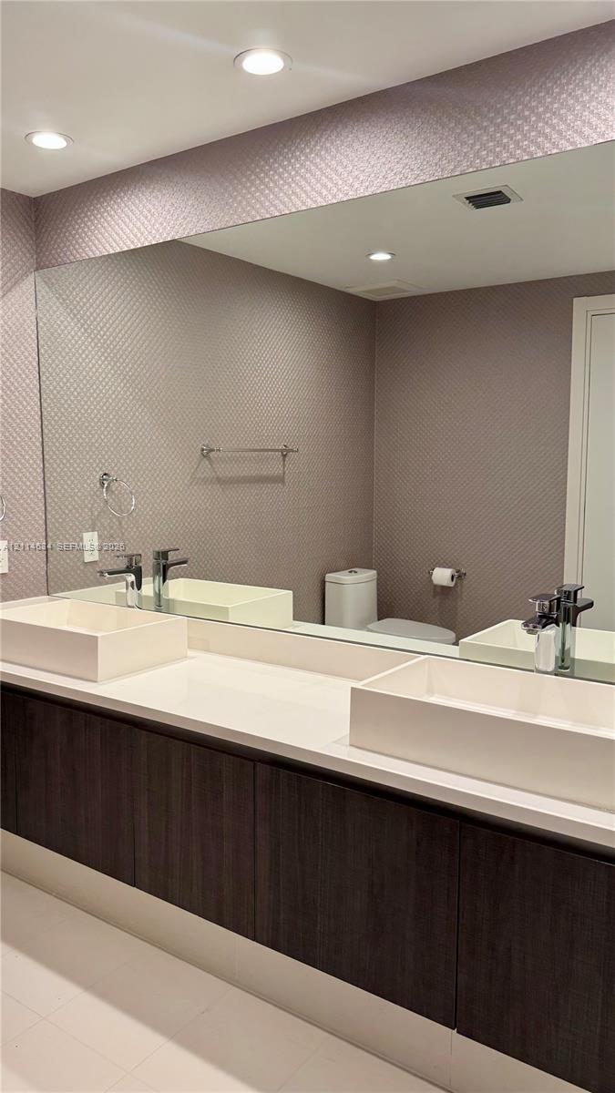 Floating vanity featuring dark wood-finish cabinetry, a dual-sink configuration with rectangular vessel basins, a continuous quartz countertop, and recessed ceiling lighting