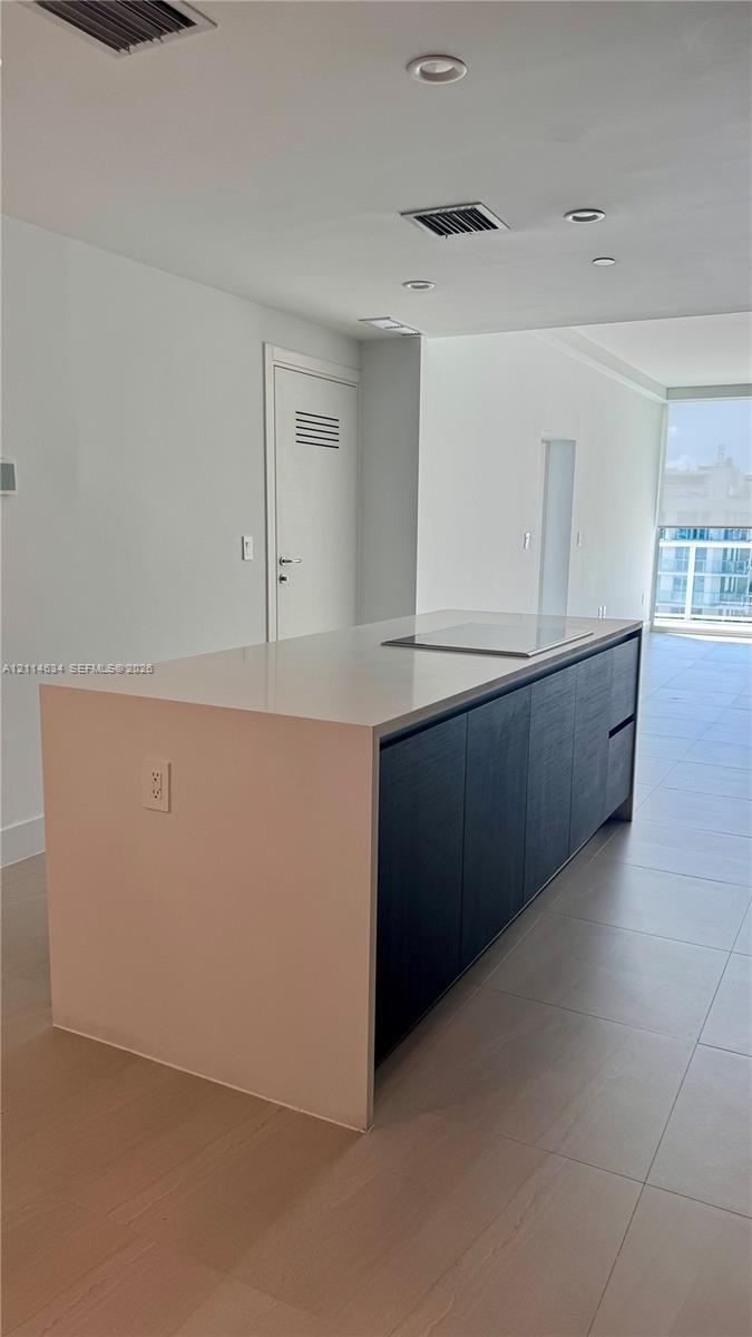 Kitchen island featuring a solid-surface countertop with an integrated cooktop and dark-finish cabinetry