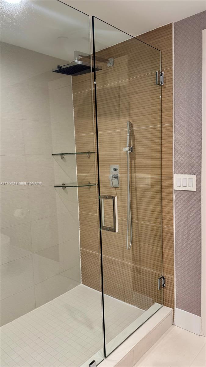 Walk-in shower featuring a glass enclosure, rainfall showerhead, handheld sprayer, horizontal-set tile wall accents, and built-in glass shelving