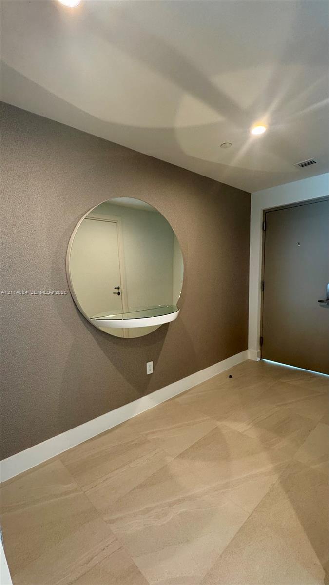 Large-format tile flooring, textured accent wall, and circular wall-mounted mirror with an integrated glass shelf