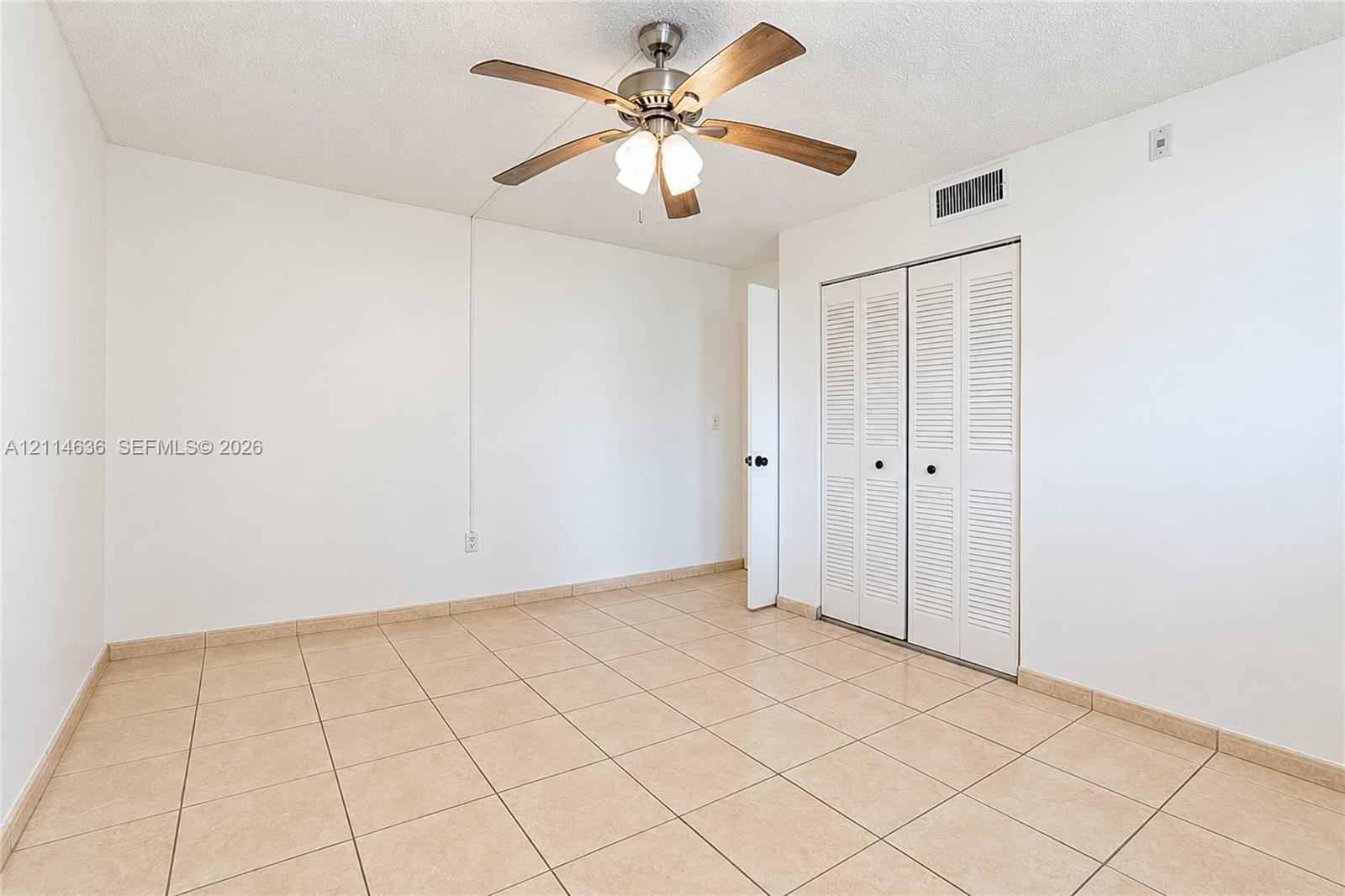 Room featuring neutral ceramic tile flooring, a brushed nickel ceiling fan with integrated lighting, and a closet with white louvered bi-fold doors