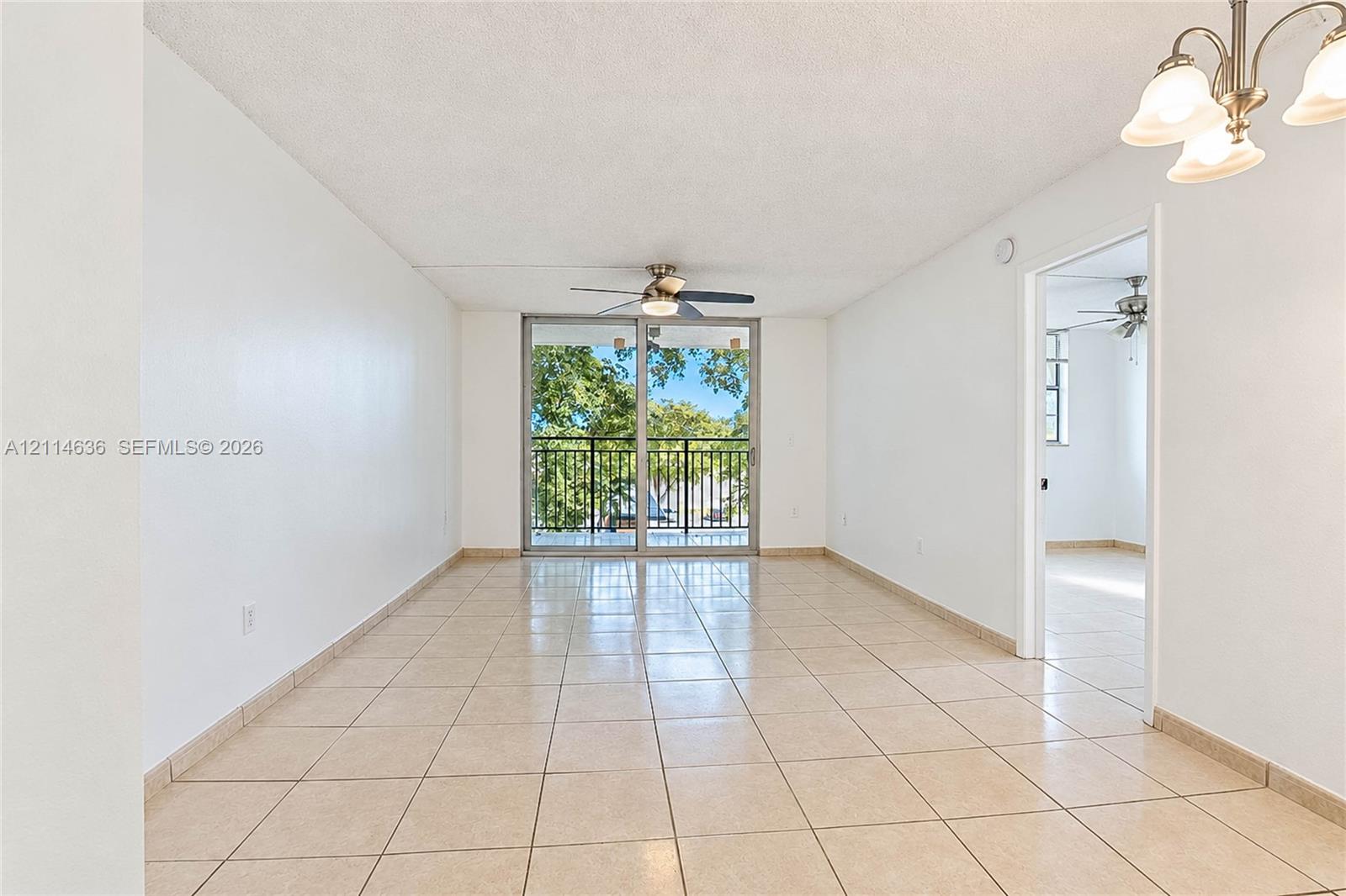 Interior space featuring large-format tile flooring, multi-light chandelier, ceiling fan, and sliding glass doors with a black metal balcony railing