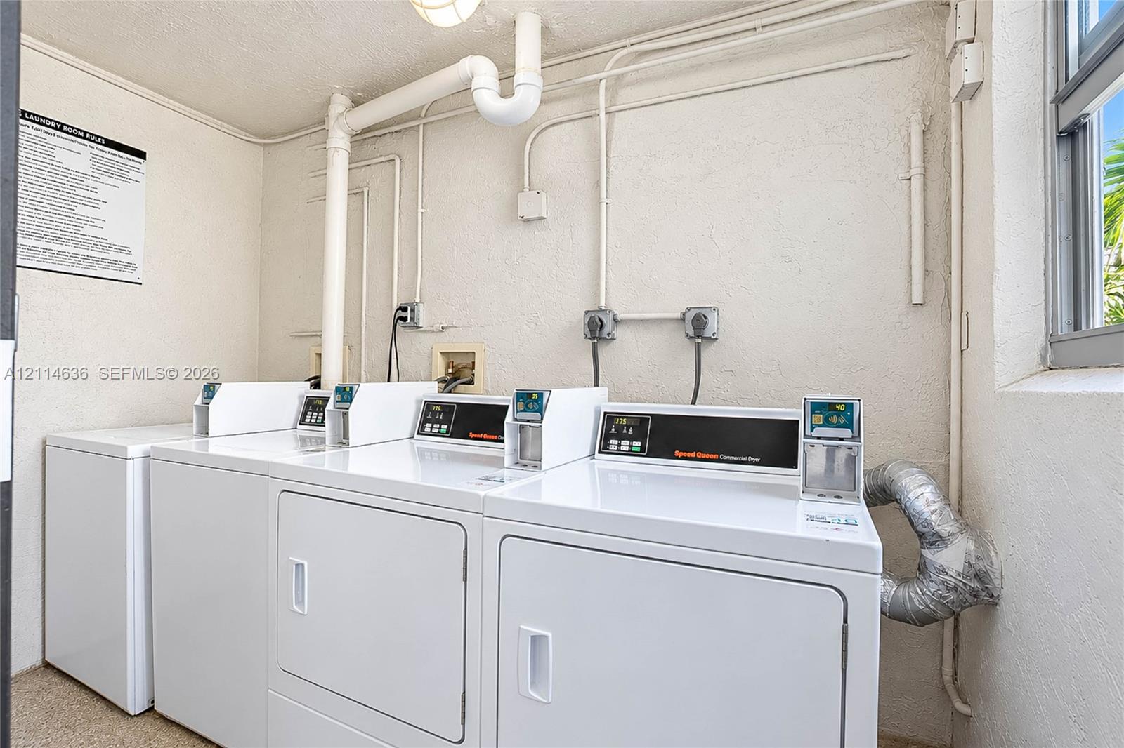 Laundry facility equipped with multiple commercial-grade dryers, wall-mounted electrical outlets, and a window