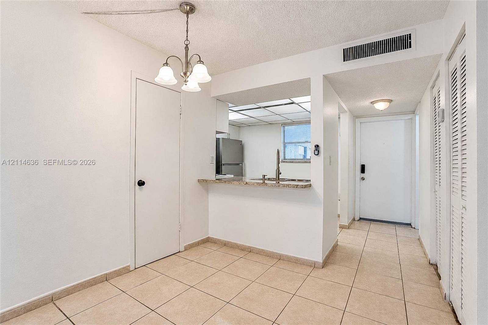 Ceramic tile flooring, three-light chandelier, stone-surface breakfast bar, stainless steel refrigerator, and louvered bi-fold closet doors