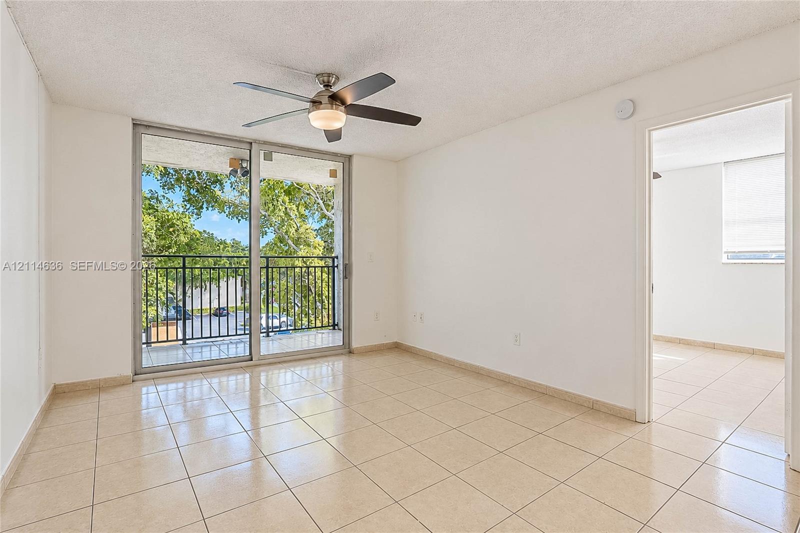 Interior featuring neutral ceramic tile flooring, sliding glass doors to a balcony, and a ceiling-mounted fan with integrated light fixture