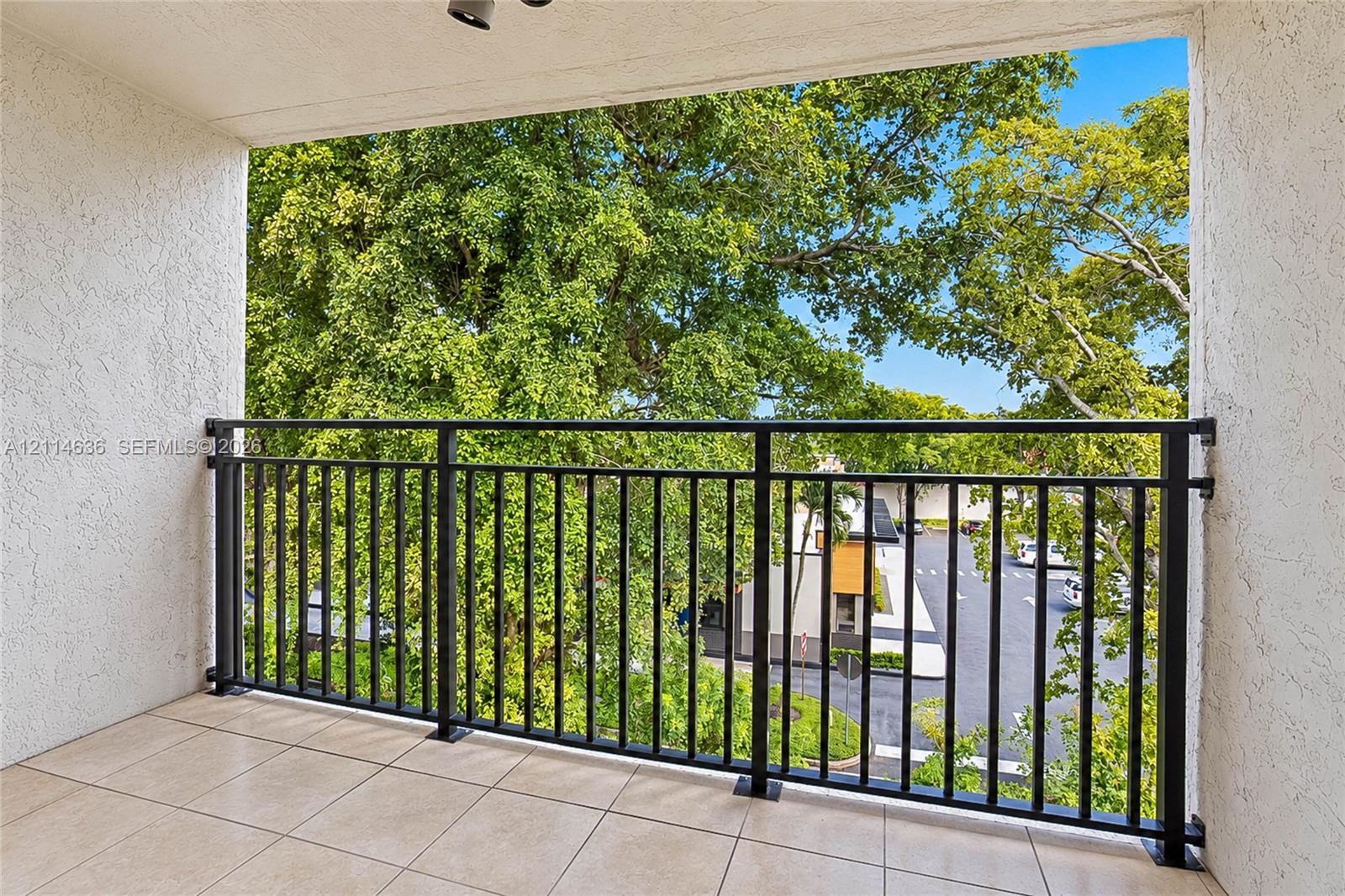 Covered balcony featuring neutral tile flooring, textured wall finishes, and a black metal railing