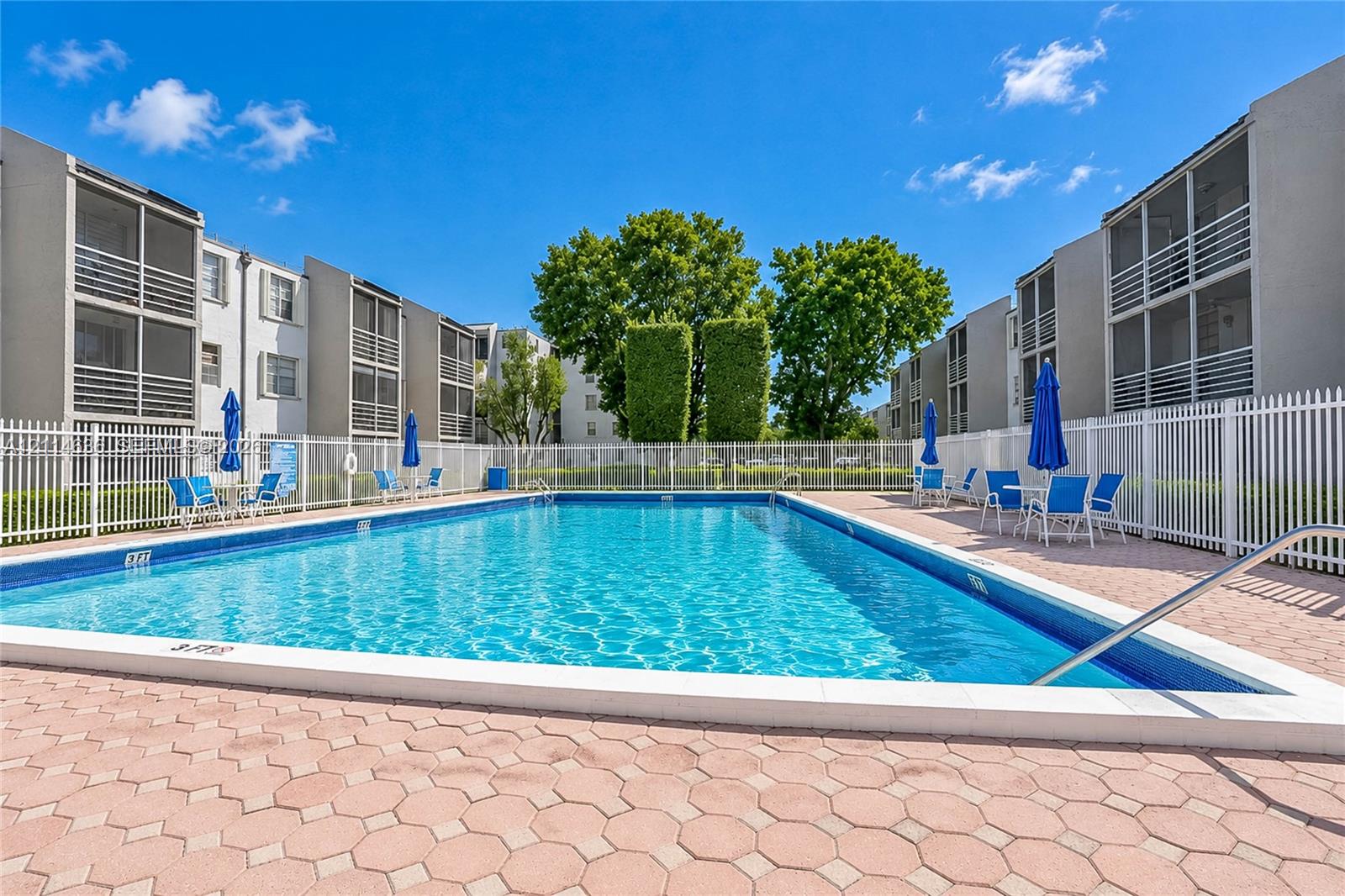Outdoor swimming pool featuring a concrete paver deck and white perimeter fencing