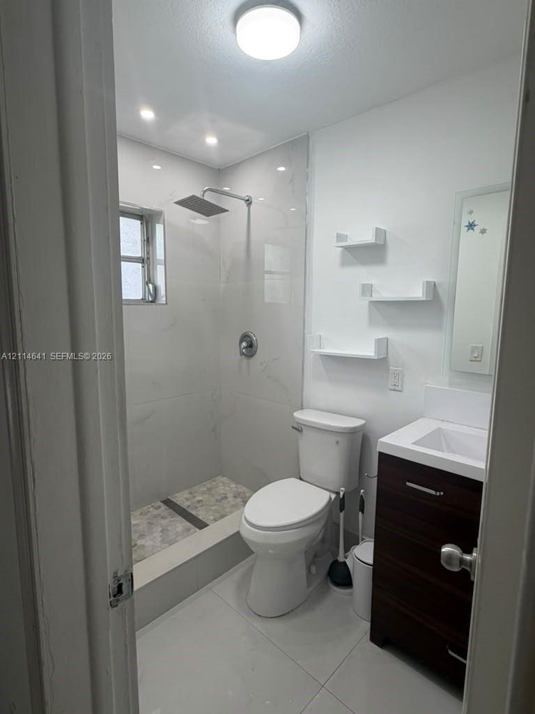 Bathroom featuring a walk-in shower with large-format wall tiles and a rainfall showerhead, stone-tiled shower floor, floating-style vanity, and built-in wall shelving