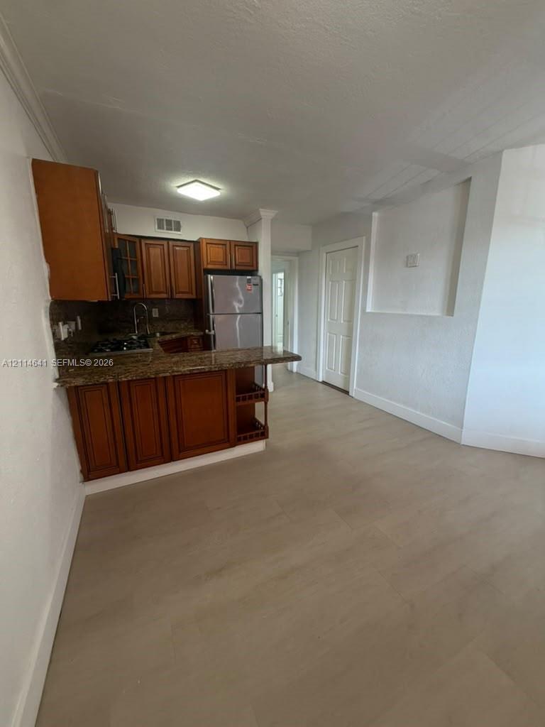 Kitchen featuring wood cabinetry, stone countertops, stainless steel refrigerator, gas cooktop, and light-toned wood-finish flooring