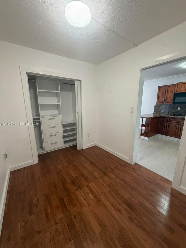 Room featuring wood-finish flooring and a custom built-in closet with integrated shelving, drawer storage, and a shoe rack