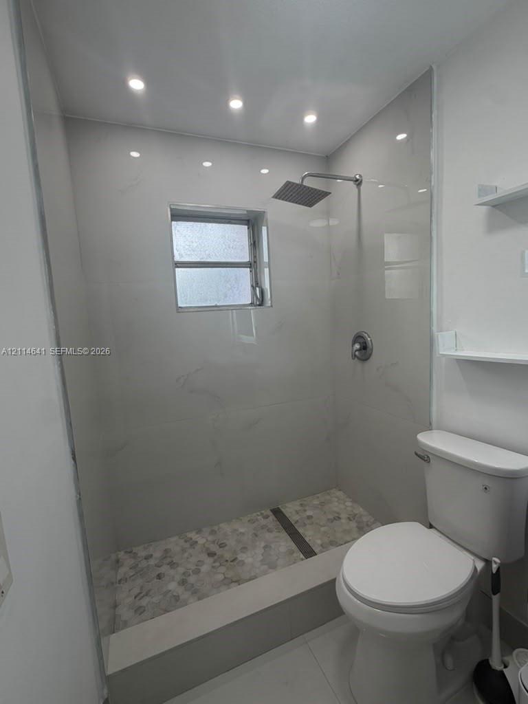 Walk-in shower featuring large-format wall tiling, stone pebble flooring, rainfall showerhead, and integrated recessed lighting