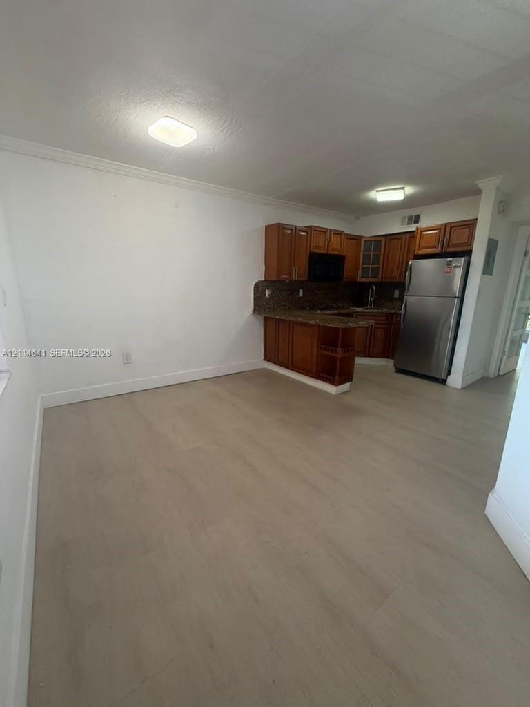 Kitchen featuring wood-finish cabinetry, stone-surface countertops, stainless steel refrigerator, and wood-finish flooring