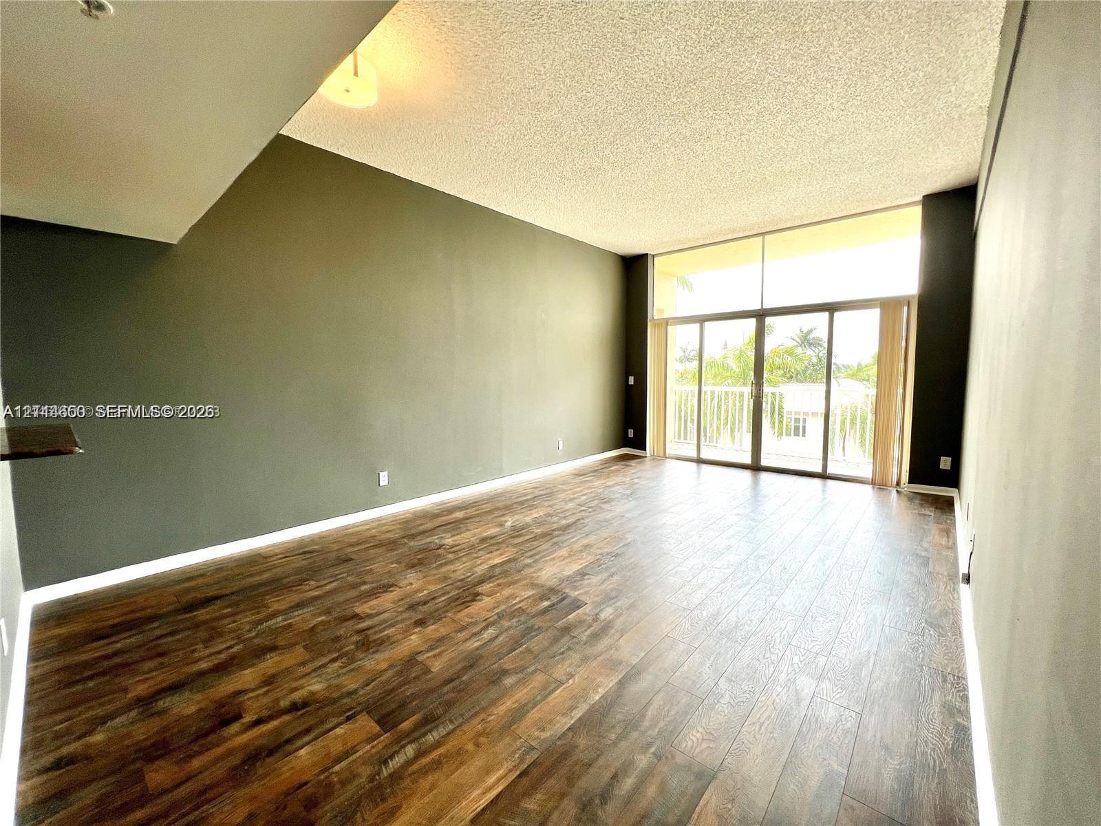 Living area featuring wood-finish flooring, floor-to-ceiling glass windows, and sliding glass doors leading to an exterior balcony