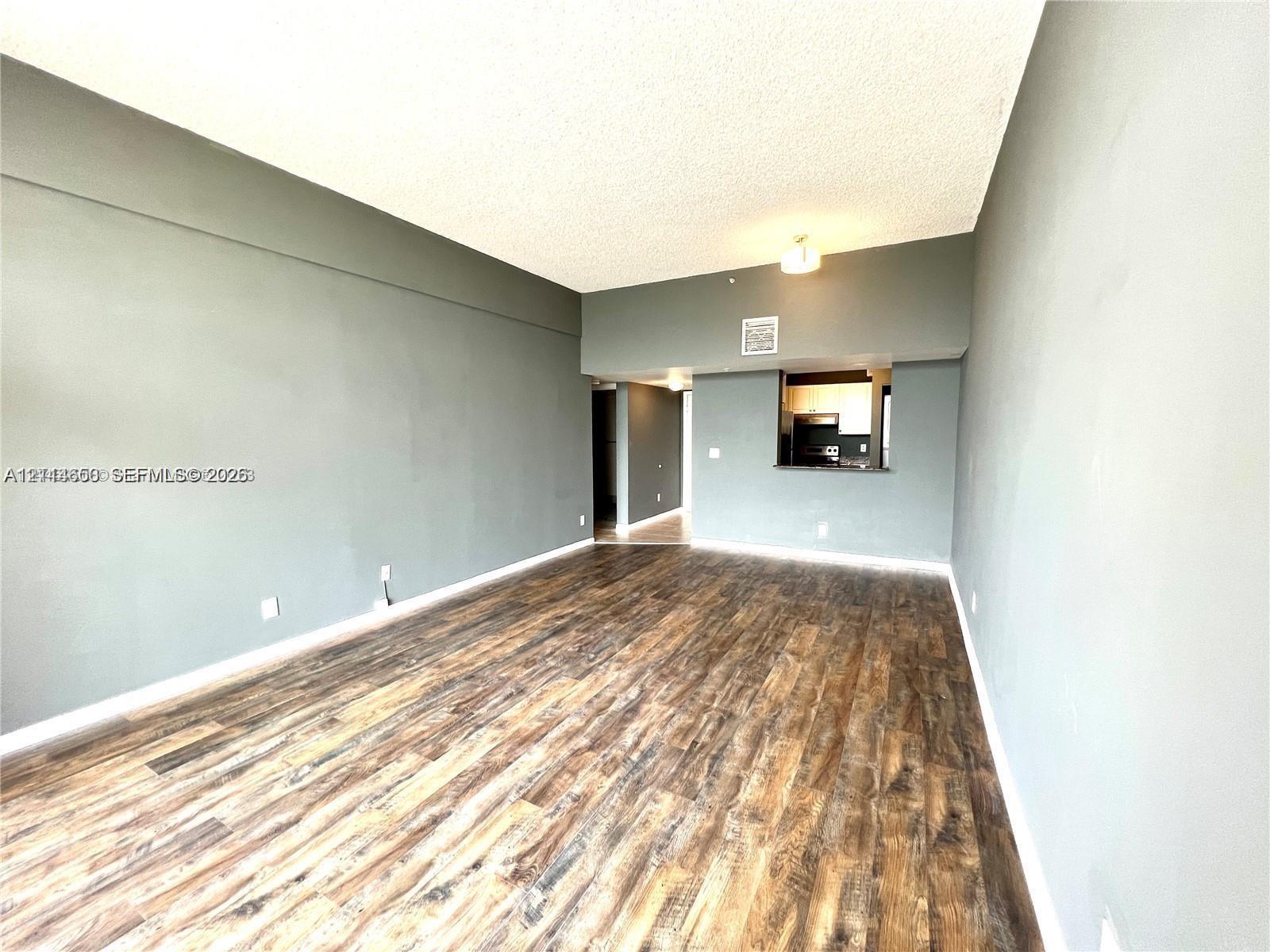 Spacious room featuring wood-finish flooring, vaulted ceilings, and a kitchen pass-through window with an integrated counter