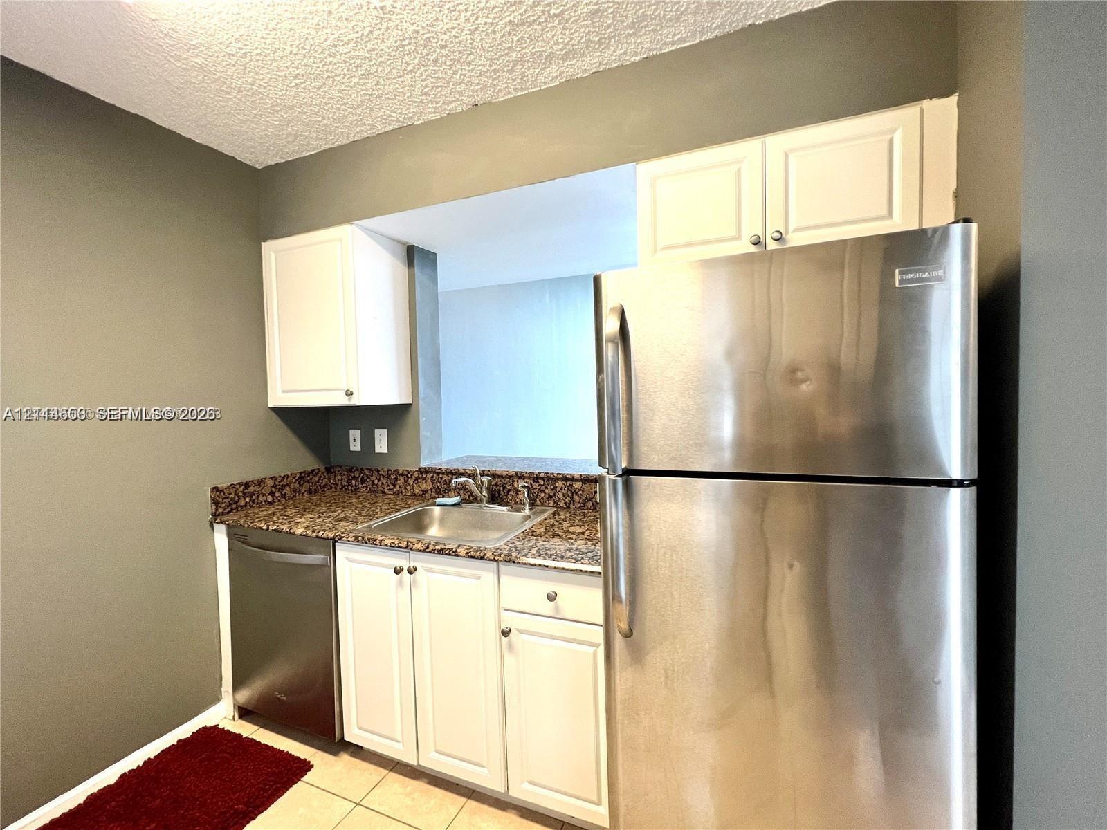 Kitchen featuring white cabinetry, stone-surface countertops, stainless steel refrigerator, stainless steel dishwasher, and a dual-basin stainless steel sink
