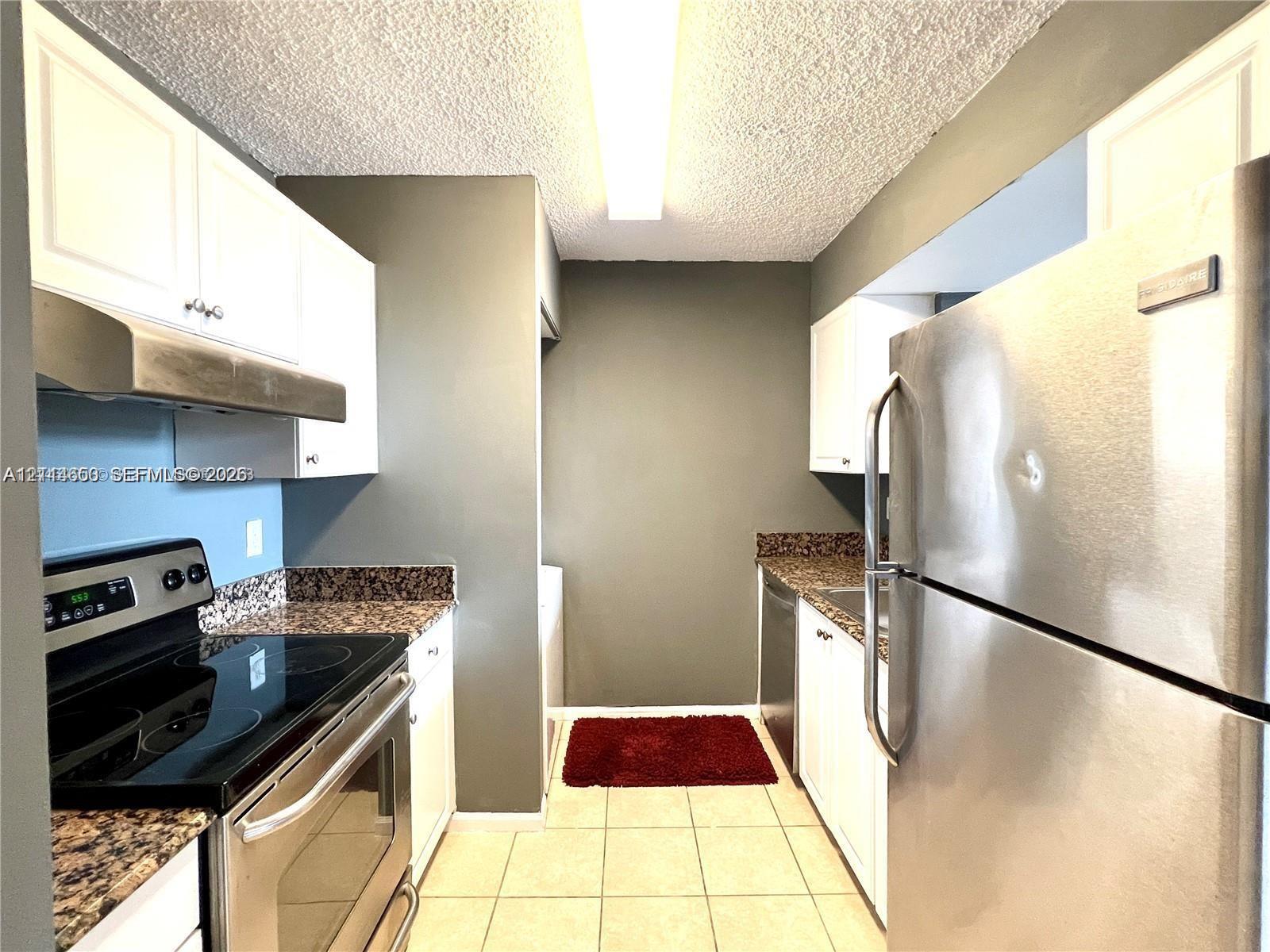 Kitchen featuring white cabinetry, stone-finish countertops, stainless steel appliances, and tile flooring