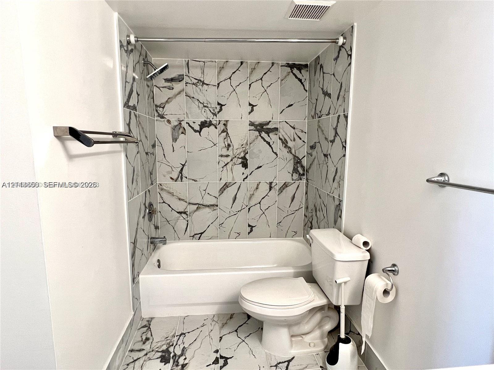 Full-height wall tiling with a high-contrast vein pattern, built-in bathtub, and chrome-finish fixtures