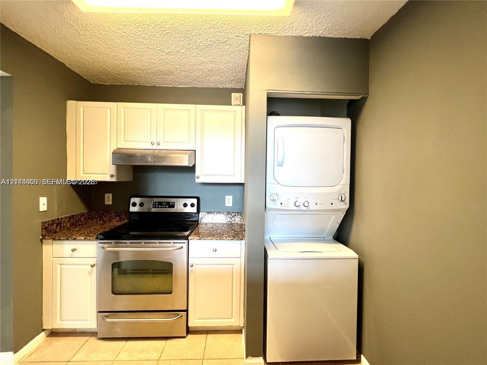 Kitchen featuring white cabinetry, stone-finish countertops, stainless steel range with integrated hood, and a stacked washer and dryer unit