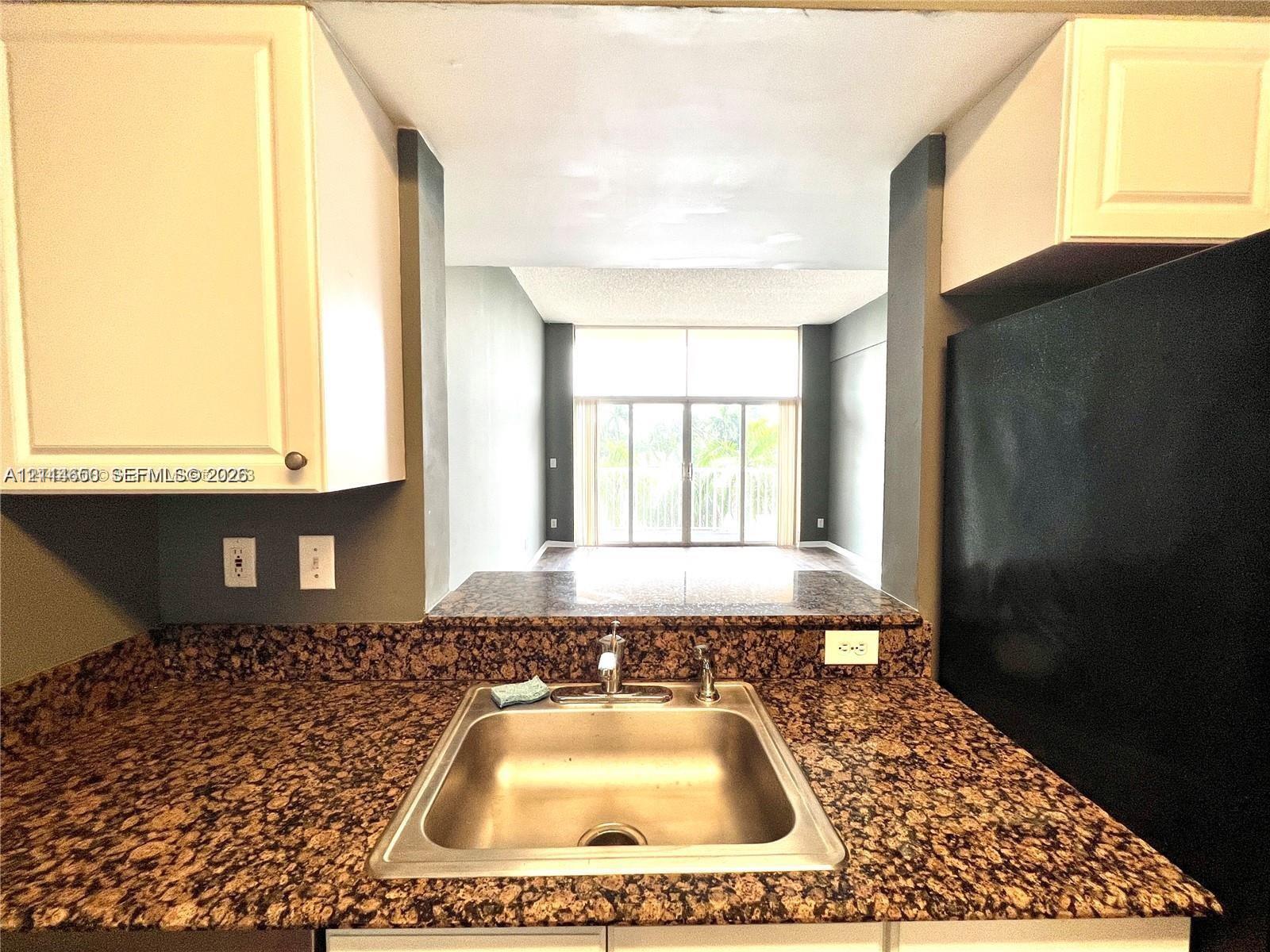 Kitchen featuring stone-finish countertops, stainless steel undermount sink, white cabinetry, and a black refrigerator
