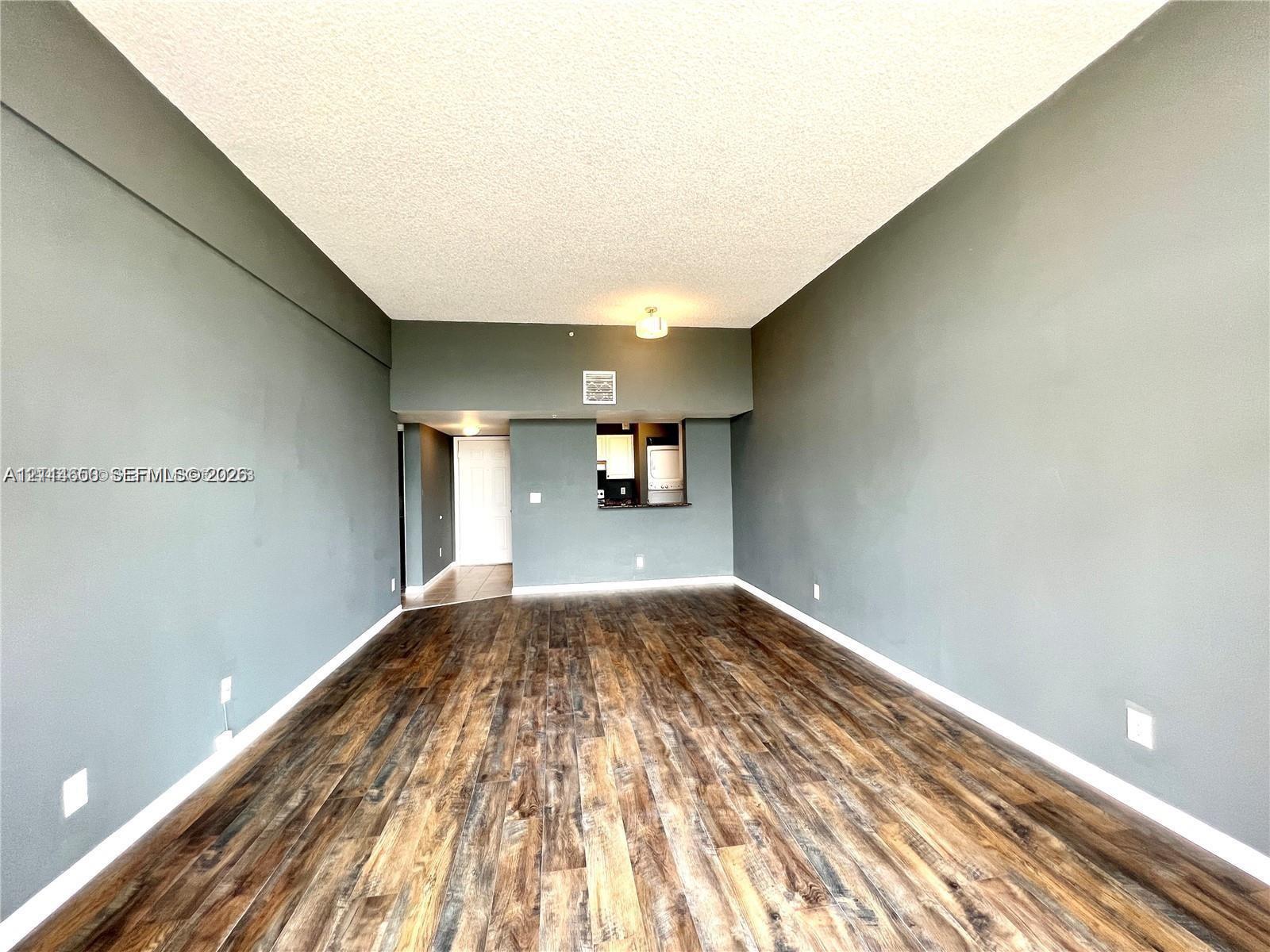 Open interior space featuring wood-finish flooring, neutral wall tones, and a pass-through opening to the kitchen area
