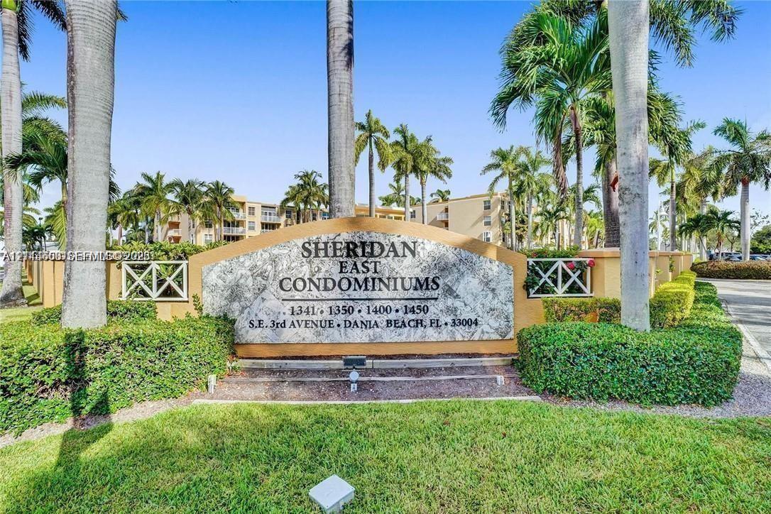 Entrance monument featuring stone-finish signage, manicured landscaping, perimeter fencing, and mature palm trees Entrance monument featuring stone-finish signage, manicured landscaping, perimeter fencing, and mature palm trees