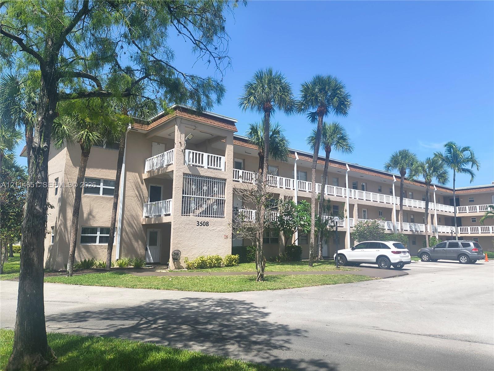 Multi-story building featuring stucco exterior, tiered balconies with white railings, and mature palm landscaping