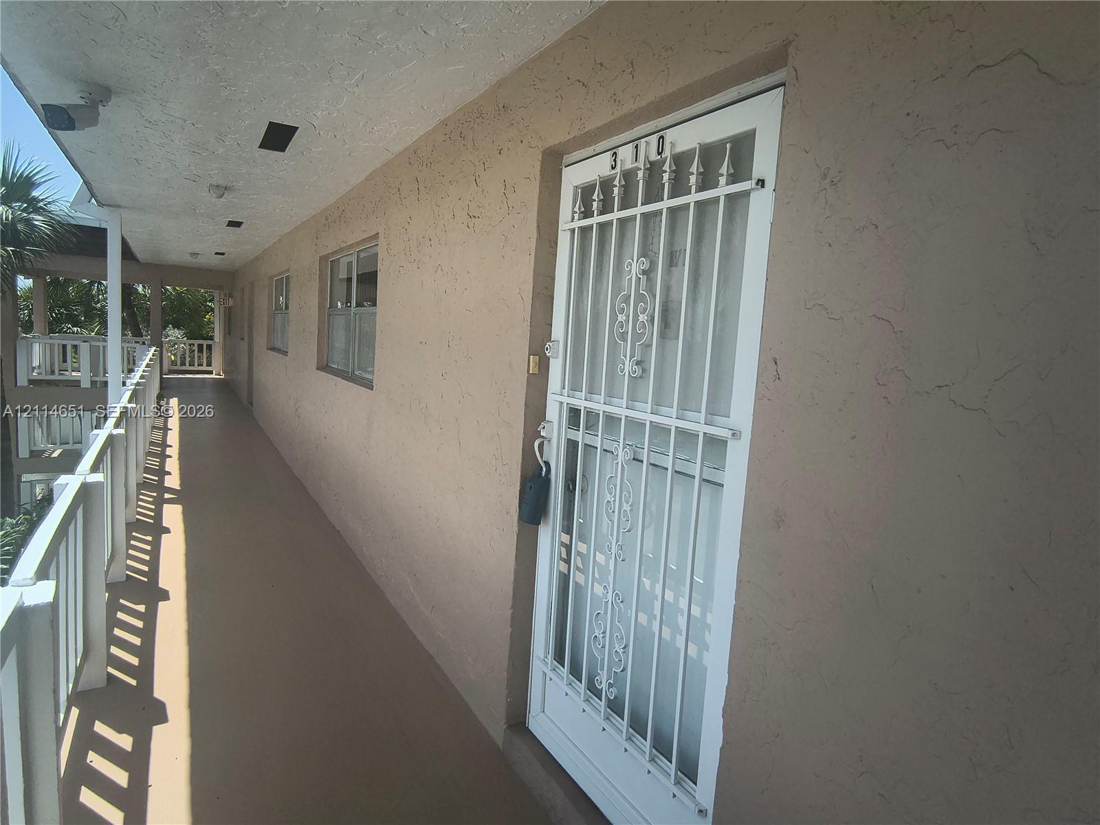 Exterior walkway featuring a stucco facade, white metal safety gate, and a white balustrade railing
