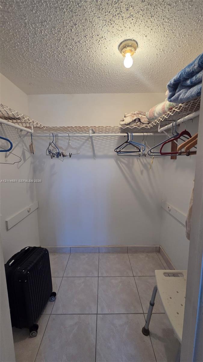 Walk-in closet featuring ceramic tile flooring, built-in wire shelving, and a ceiling-mounted light fixture Walk-in closet featuring ceramic tile flooring, built-in wire shelving, and a ceiling-mounted light fixture