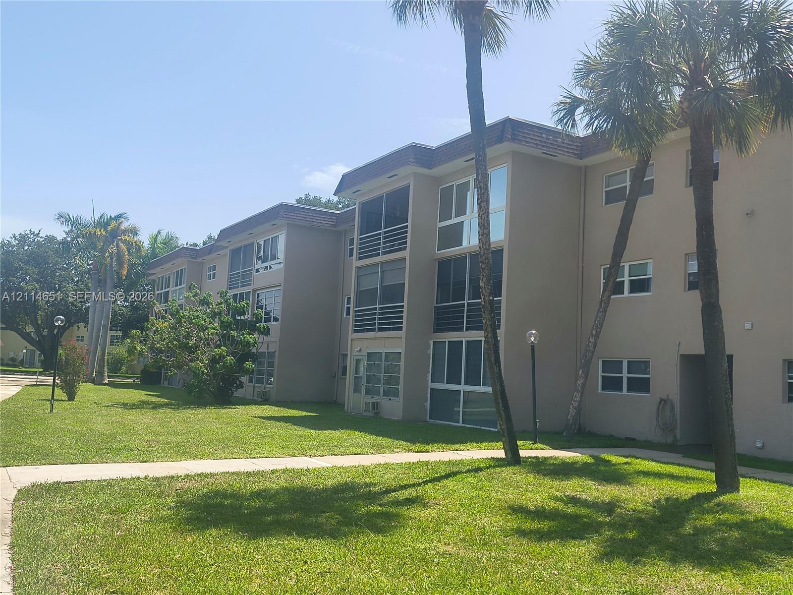 Multi-story stucco exterior featuring screened balconies and mature palm trees