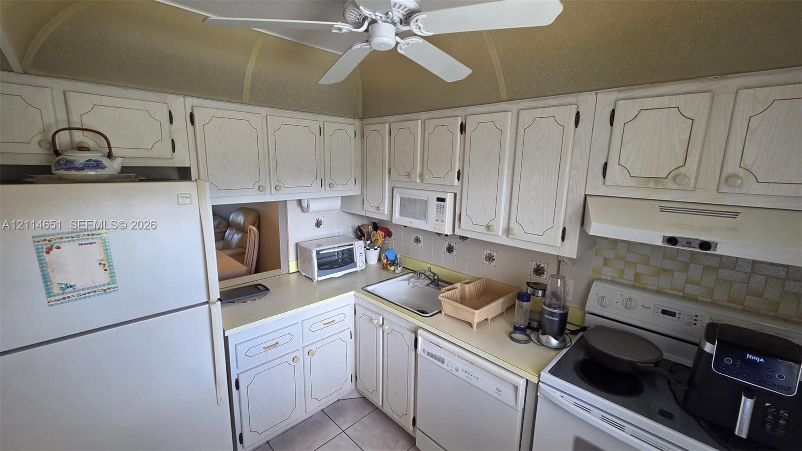 Kitchen featuring white raised-panel cabinetry, light-toned countertops, tile backsplash, built-in microwave, and ceiling fan Kitchen featuring white raised-panel cabinetry, light-toned countertops, tile backsplash, built-in microwave, and ceiling fan