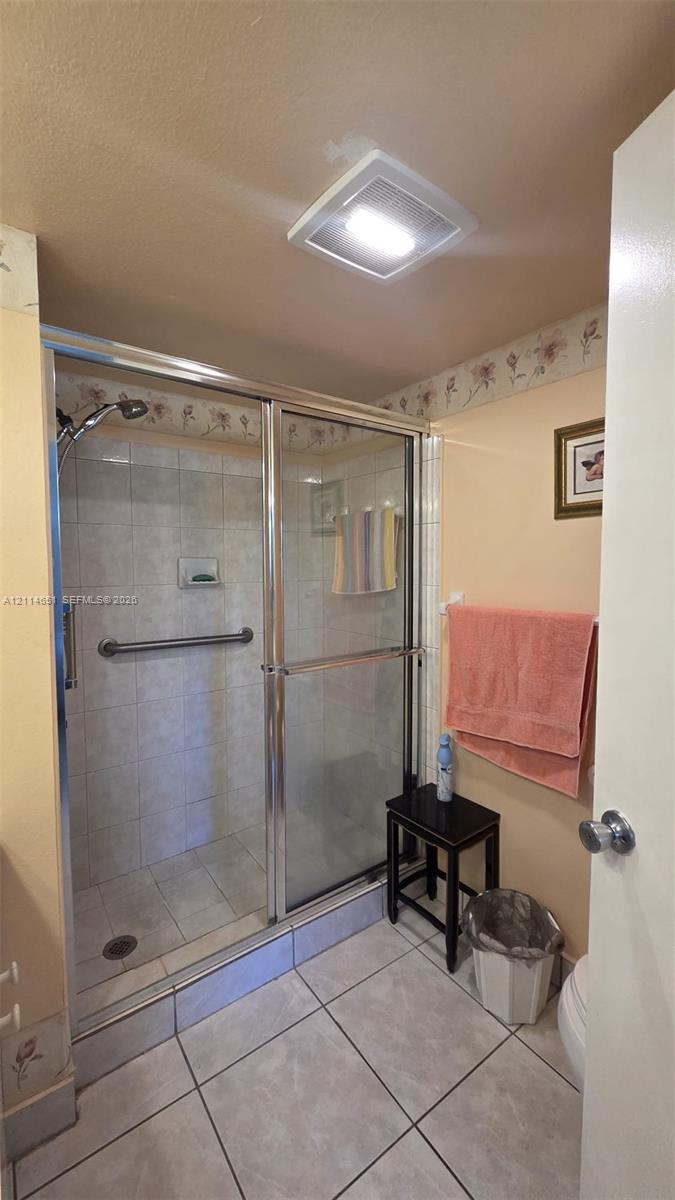 Shower stall featuring a glass-enclosed frame, tiled walls with a built-in recessed soap niche, a mounted metal grab bar, and large-format tile flooring Shower stall featuring a glass-enclosed frame, tiled walls with a built-in recessed soap niche, a mounted metal grab bar, and large-format tile flooring