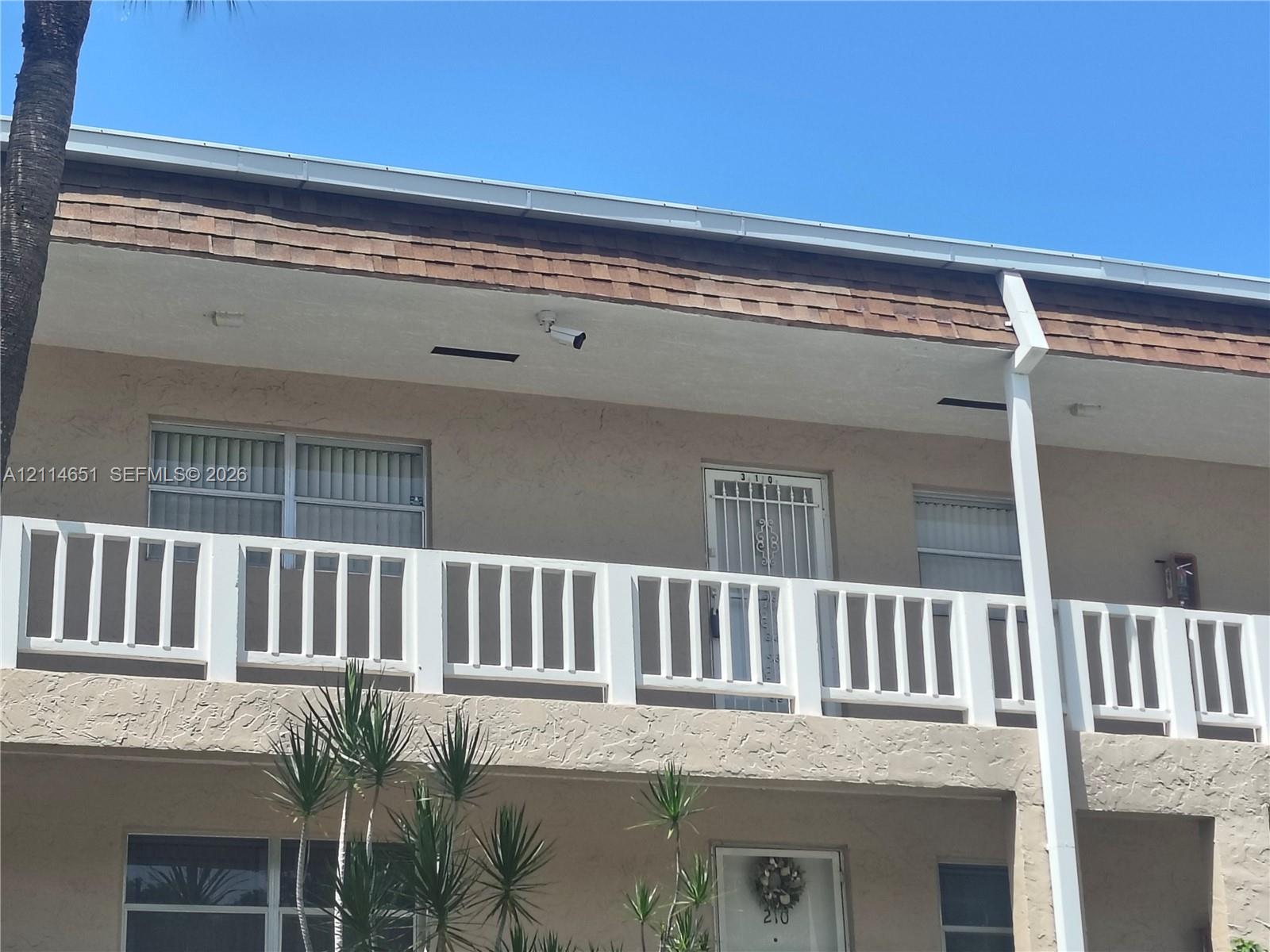 Stucco exterior featuring a second-story balcony with white railing, asphalt shingle roofing, and vertical sliding windows