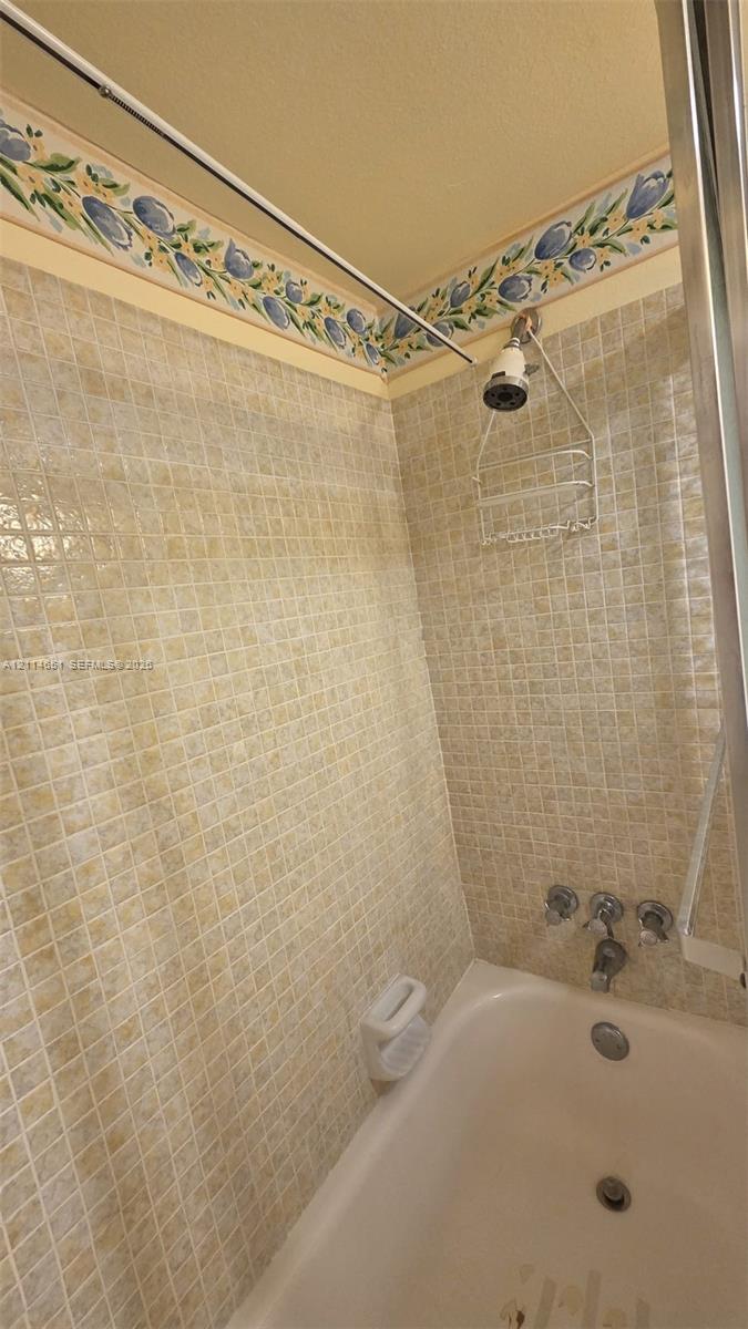 Bathtub enclosure featuring mosaic tile surround, floral decorative border, metal shower head, and chrome three-handle plumbing fixtures
