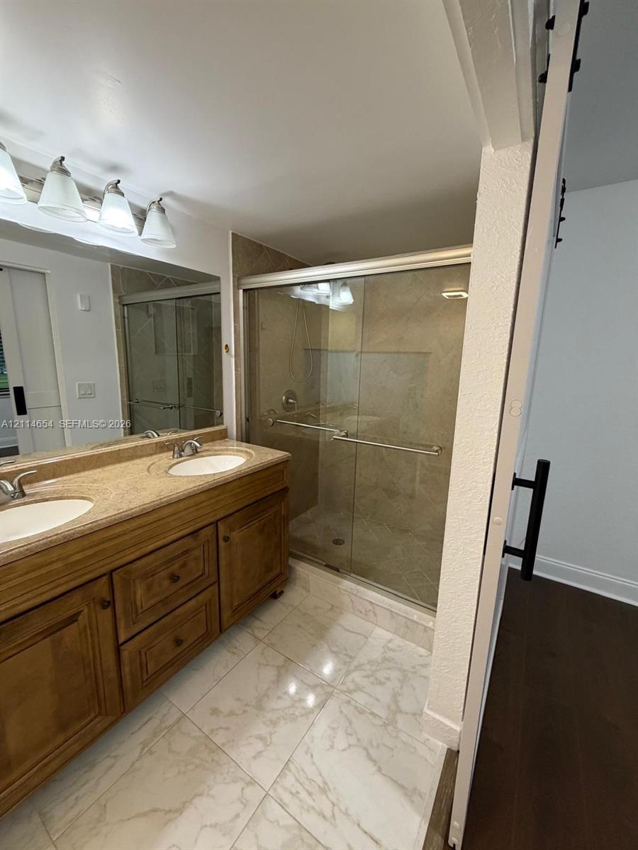 Dual-sink vanity with stone-finish countertop, walk-in shower with sliding glass doors, tile flooring, and integrated wall-mounted sliding door hardware