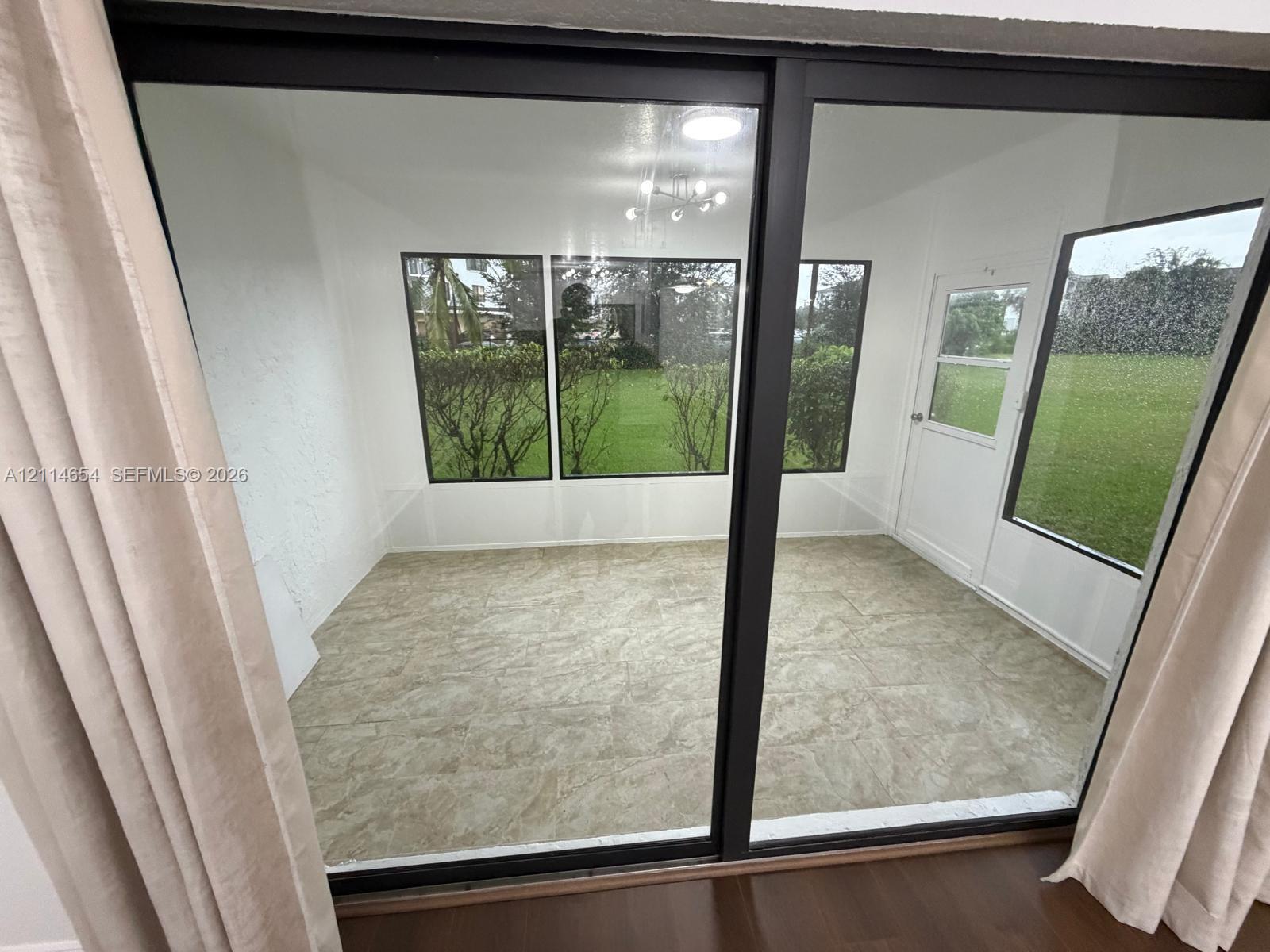 Enclosed sunroom featuring large-format stone-tile flooring, expansive multi-pane windows, and a dedicated exterior access door