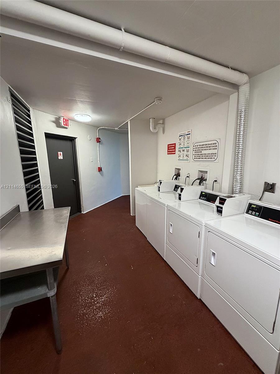 Laundry room featuring multiple white front-loading clothes washers and dryers, a stainless steel folding table, and solid-surface flooring