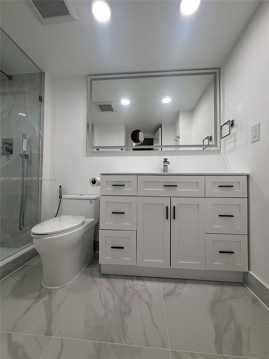 Walk-in shower featuring large-format stone-finish tile surround, frameless glass enclosure, rainfall showerhead, and hexagonal floor tiling