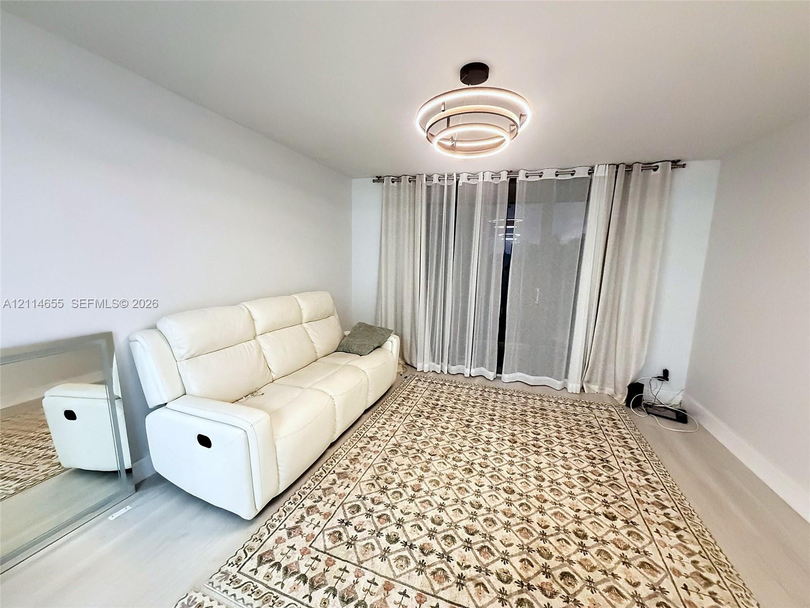 Modern interior space featuring light-toned wood-finish flooring, a tiered circular LED flush-mount fixture, and full-height sliding glass doors