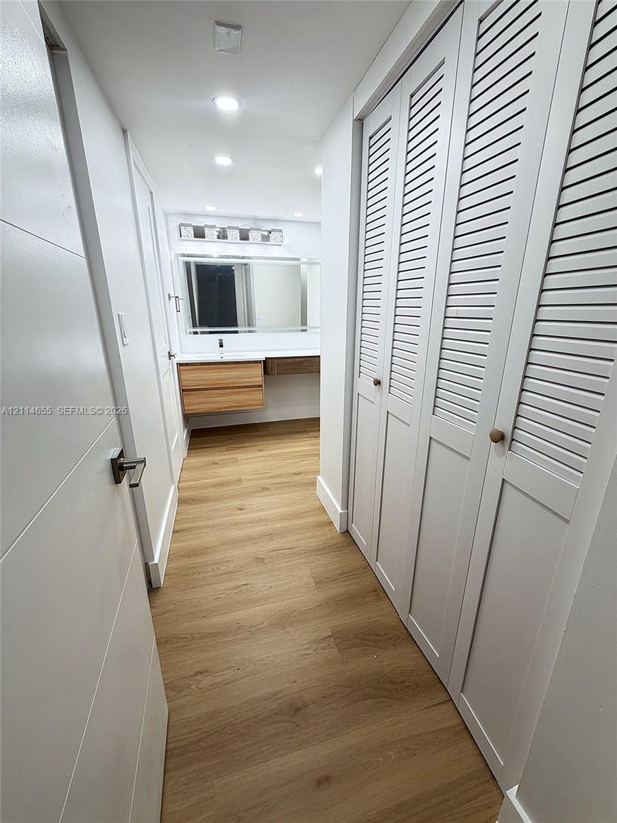 Wood-finish flooring, dual-door louvered closets, wall-mounted floating vanity, and integrated vanity lighting