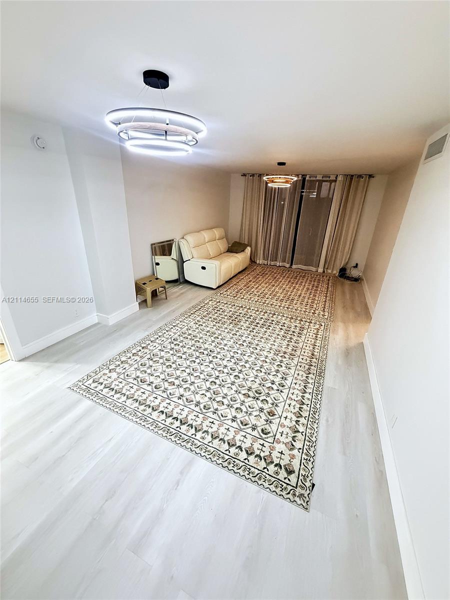 Interior room featuring light-toned wood-finish flooring, two modern multi-tier LED light fixtures, and floor-to-ceiling curtain panels