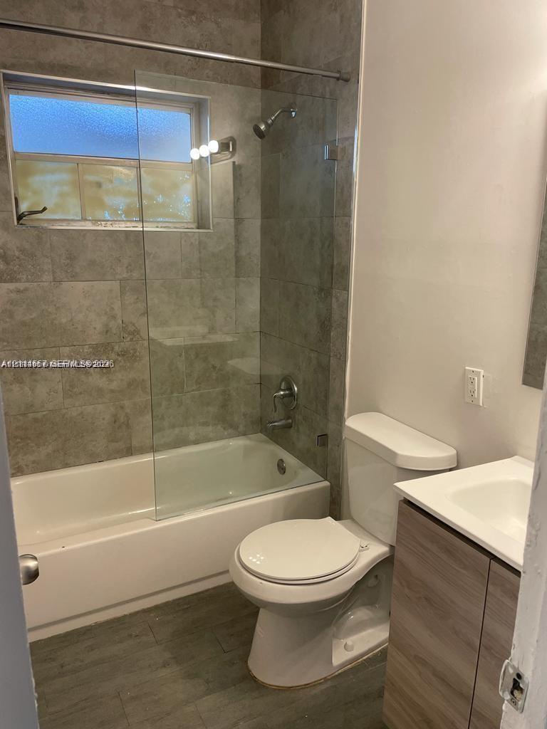 Bathroom featuring large-format tile shower surround, frameless glass shower panel, wood-finish vanity with integrated sink, and wood-finish flooring