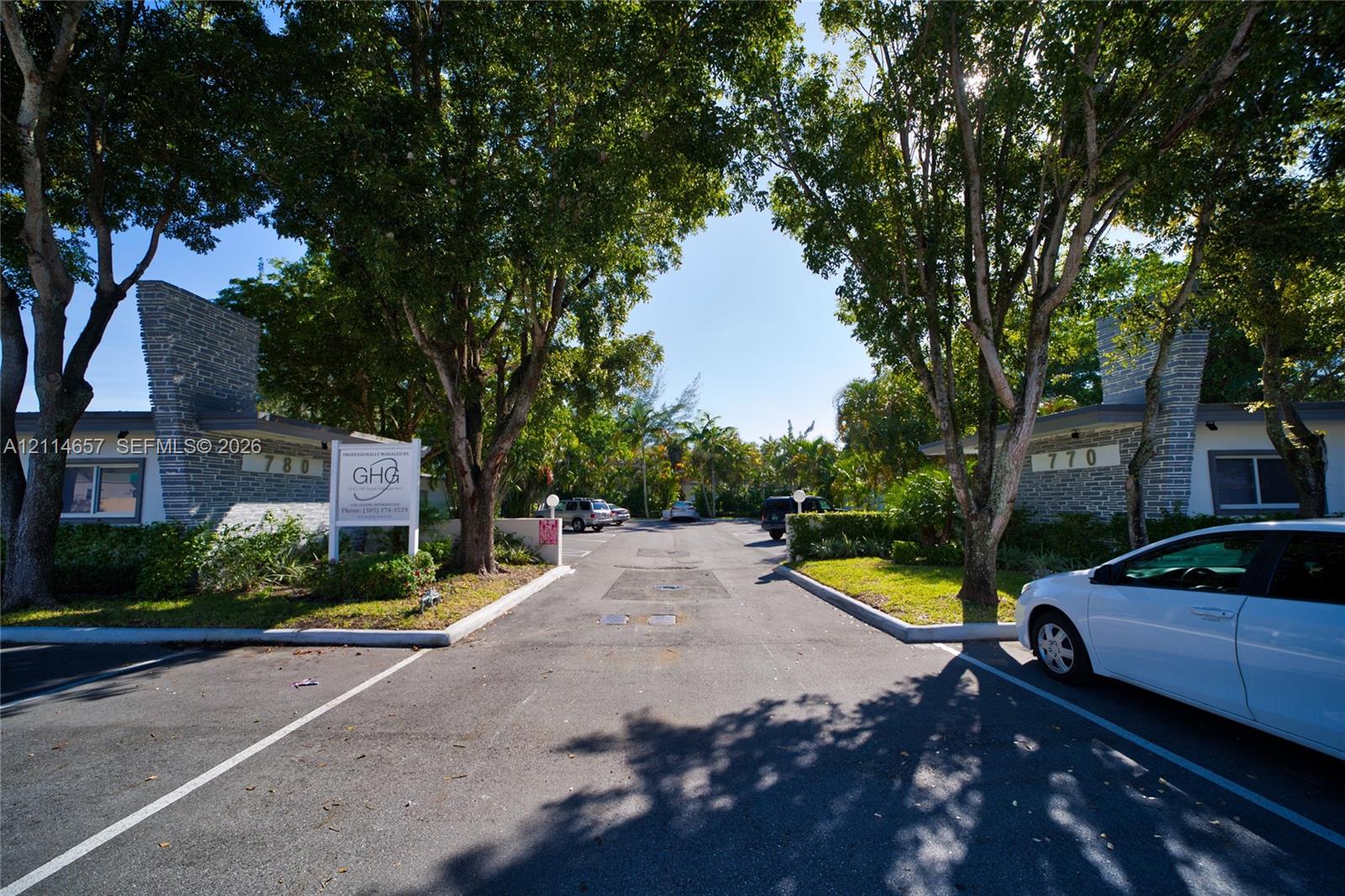Exterior facade featuring textured stone pillars, mature canopy trees, and paved parking area