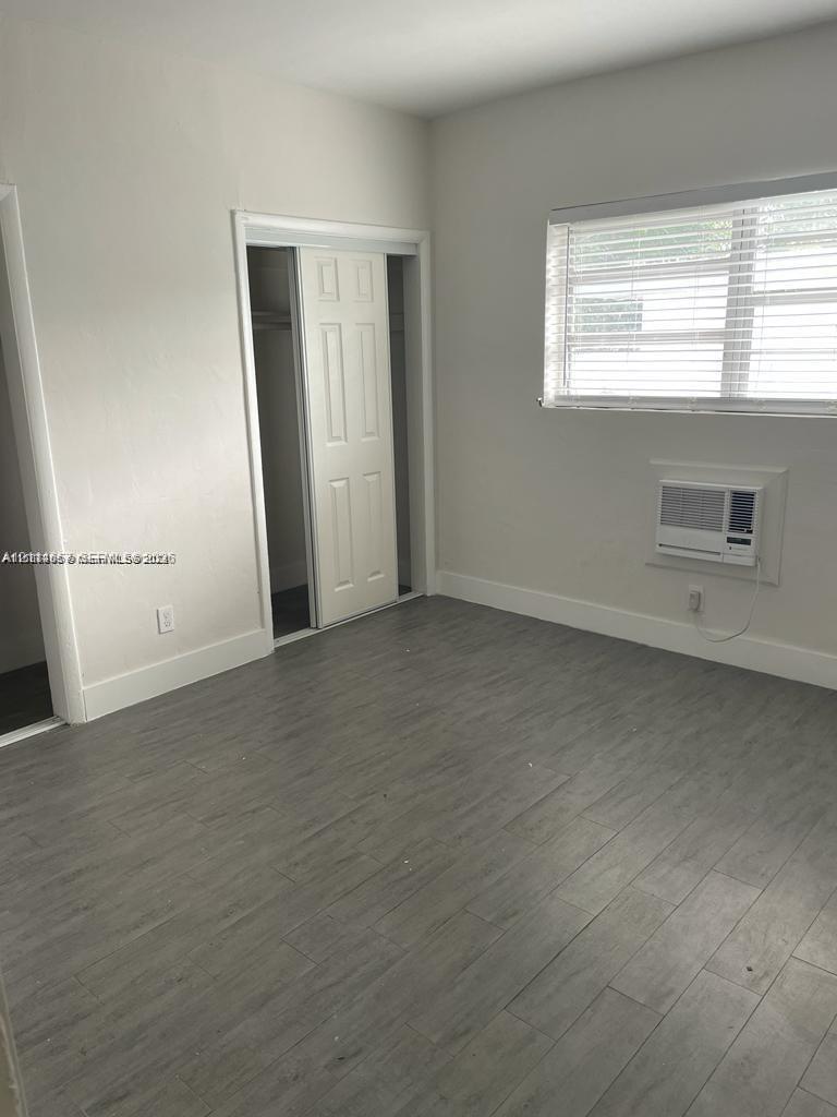 Neutral interior space featuring wood-finish flooring, a wall-mounted climate control unit, and a built-in closet with double-panel doors