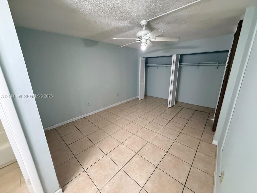 Square tile flooring, ceiling fan with light fixture, and reach-in closet with double bifold doors