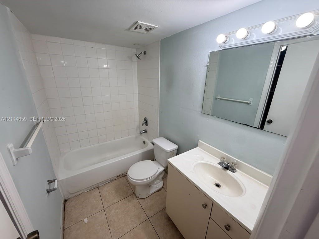 Bathroom featuring tile flooring, a tub-shower combination with full-height tile surround, vanity with integrated basin, and wall-mounted vanity lighting