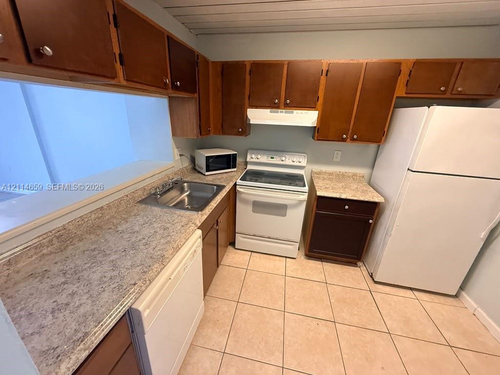 Kitchen featuring medium-toned wood cabinetry, stone-patterned laminate countertops, white appliance suite, and ceramic tile flooring