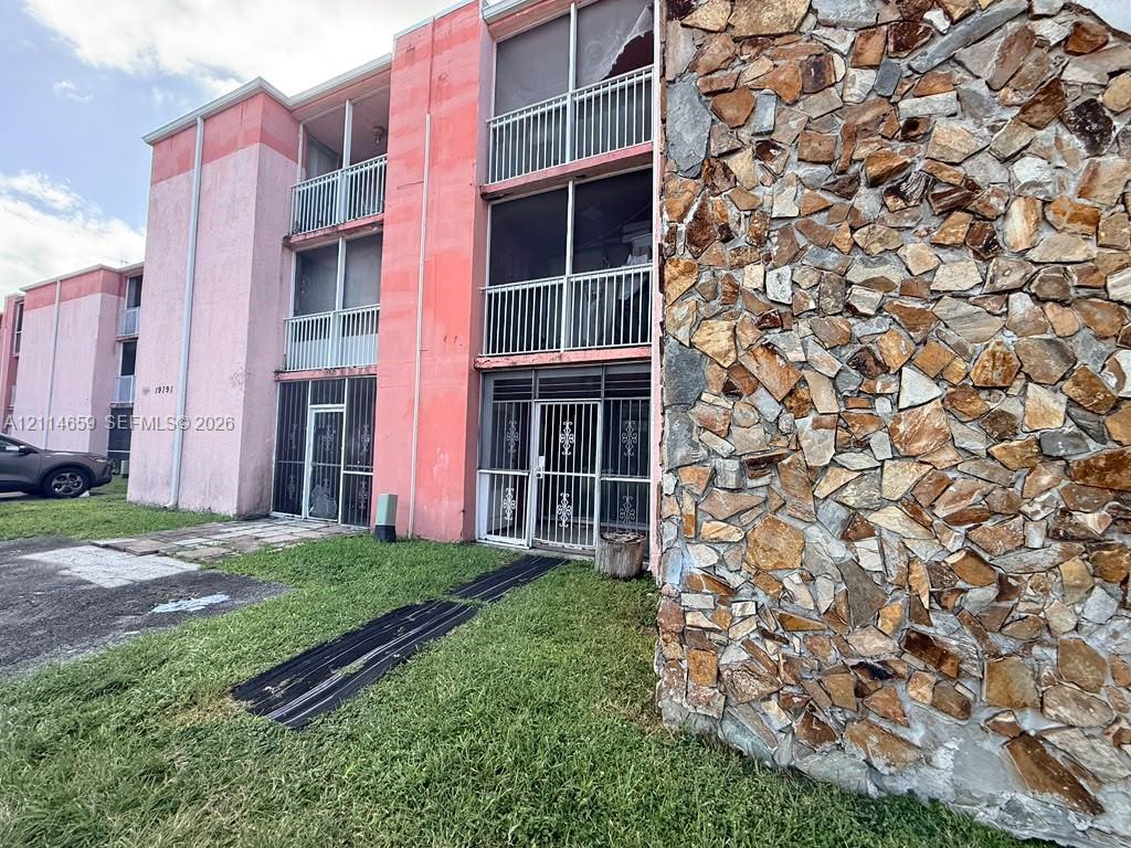 Multi-story exterior featuring decorative natural stone masonry, private screened-in balconies with metal railings, and metal security door frames