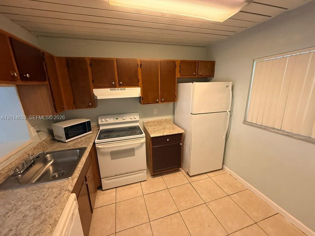 Kitchen featuring wood cabinetry, stone-finish laminate countertops, ceramic tile flooring, and a flat-panel ceiling