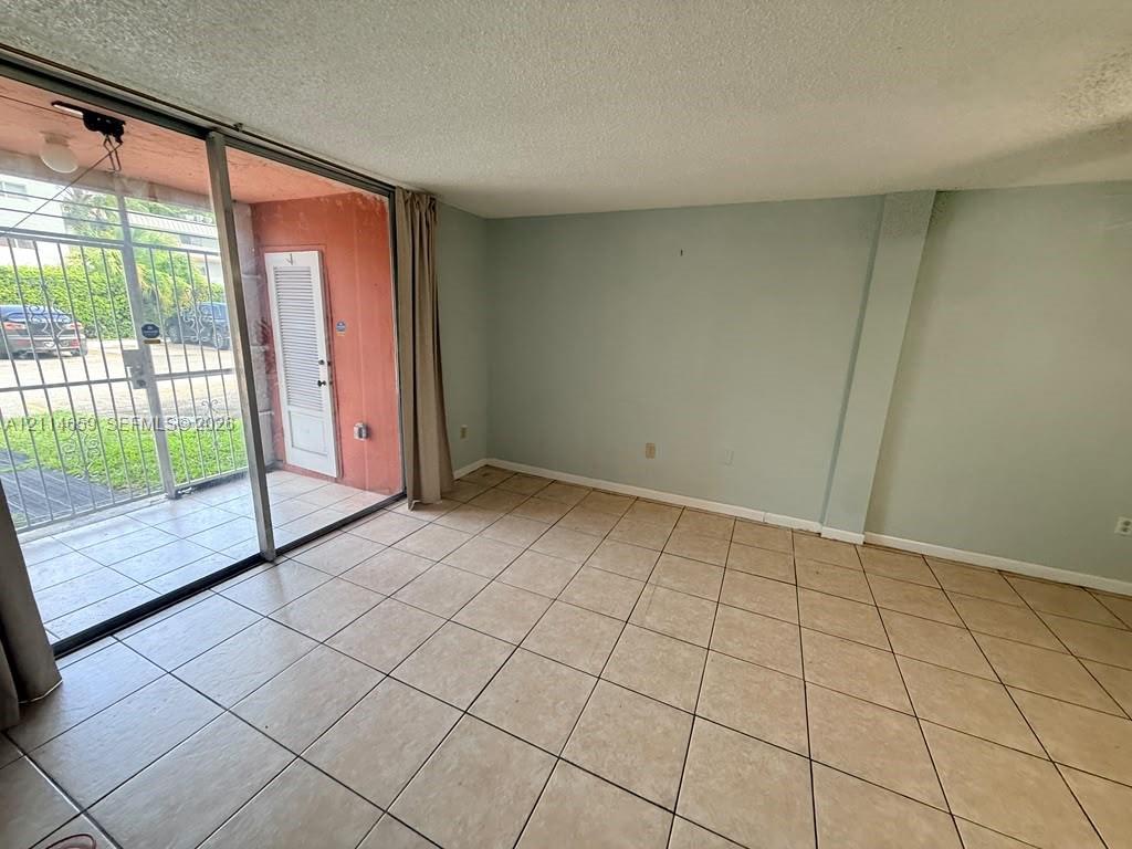 Interior space featuring large-format ceramic tile flooring, sliding glass patio door, and exterior metal security gate